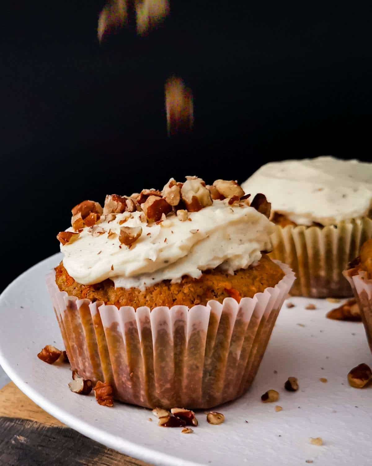 Food photography action shot:Keto Carrot Cupcake frosted with crushed pecans dropping over top