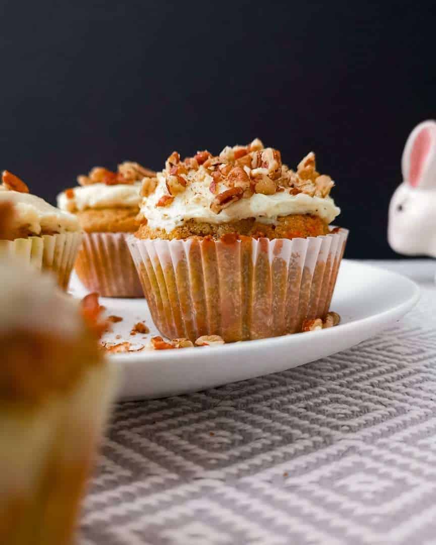 Low carb carrot cake cupcakes, frosted on a plate with the Easter bunny sneaking into frame