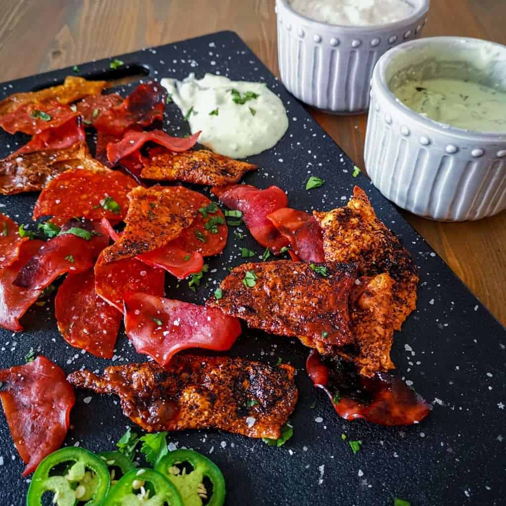 A variety of homemade low carb keto friendly meat chips on a platter with dip