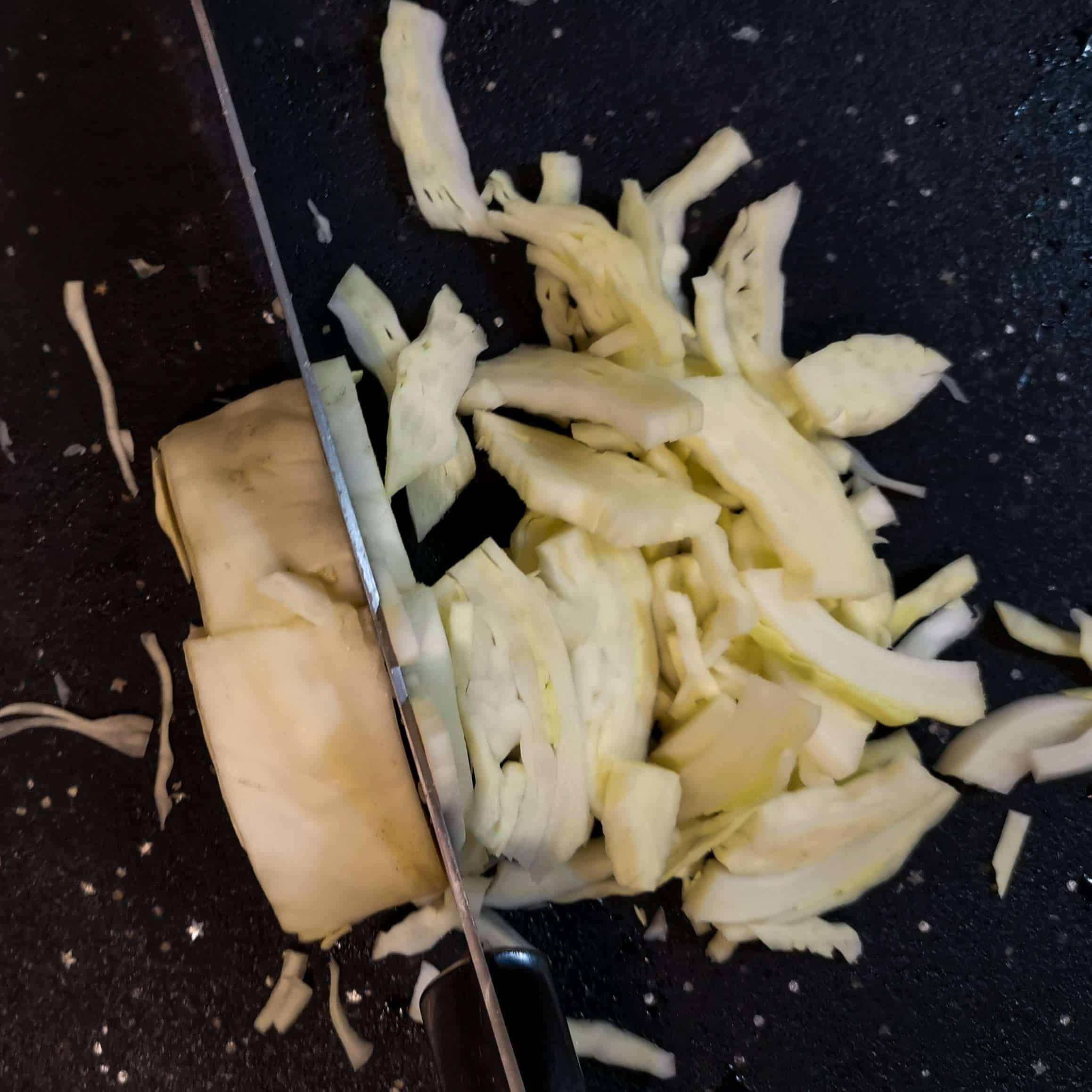 White Cabbaged Sliced finely with a knife on a cutting board
