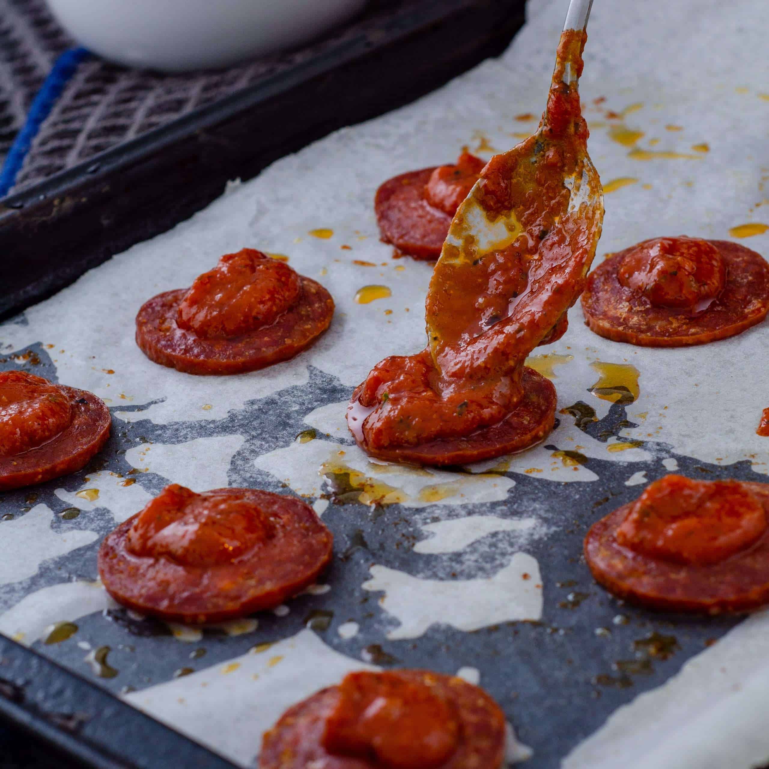 Low Carb Pizza sauce being spread on salami crust