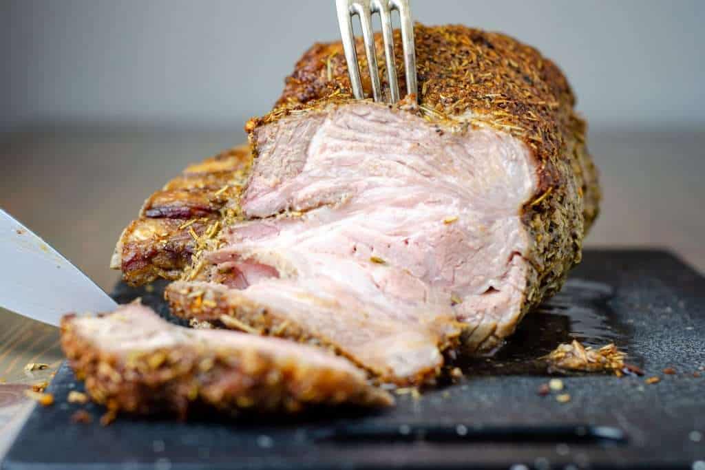 Herb Crusted keto pork roast being sliced on a cutting board