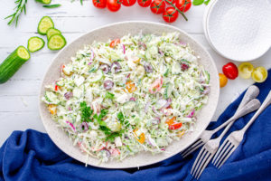 Creamy Greek Coleslaw on a oval dish surrounded by ingredients