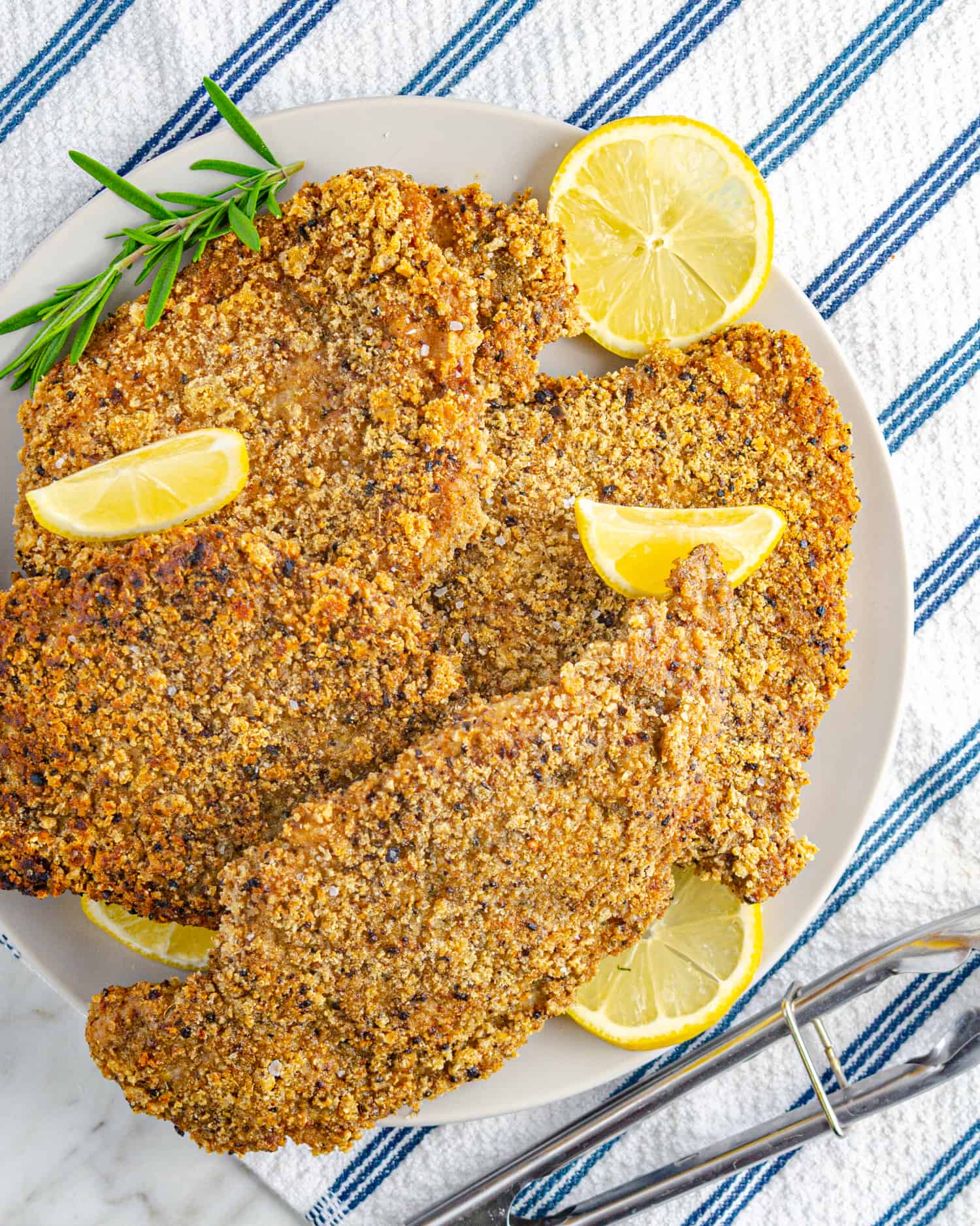 Pork schnitzel piled on a plate with lemon wedges