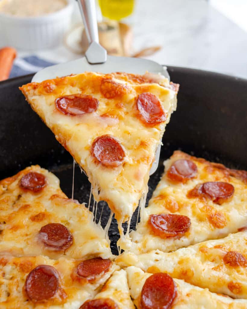 Cheese pull shot of chicken crust pizza lifting out of a skillet.