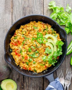 Spicy Tex-Mex Scrambled eggs garnished with jalapeno, avocado, and cilantro in a cast iron skillet.