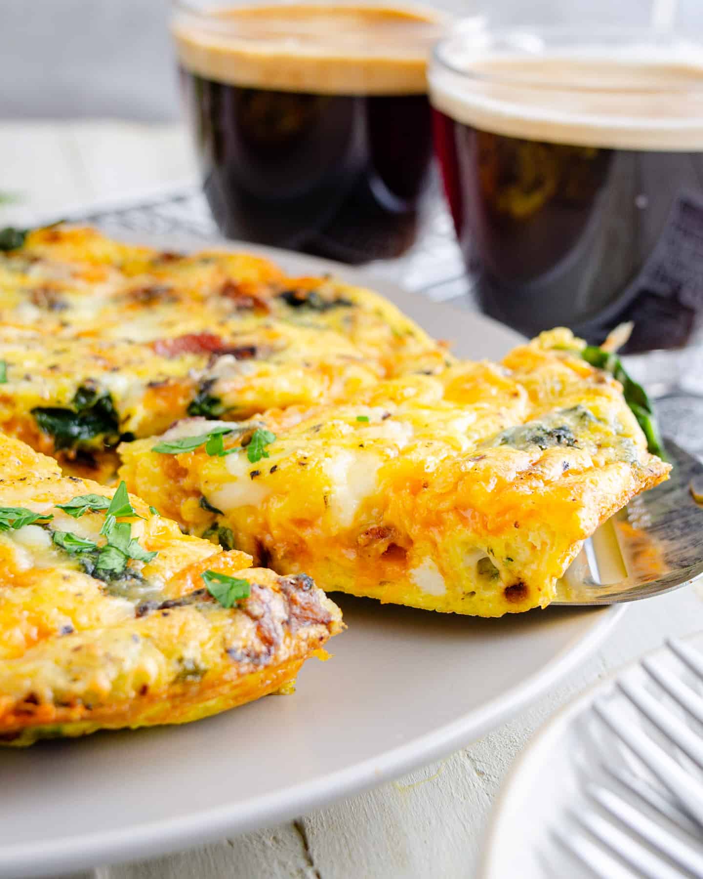 A slice of baked frittata with lattes in the background.