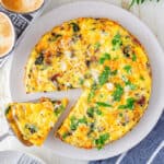A baked keto frittata on a plate, a slice being taken out with a spatula.