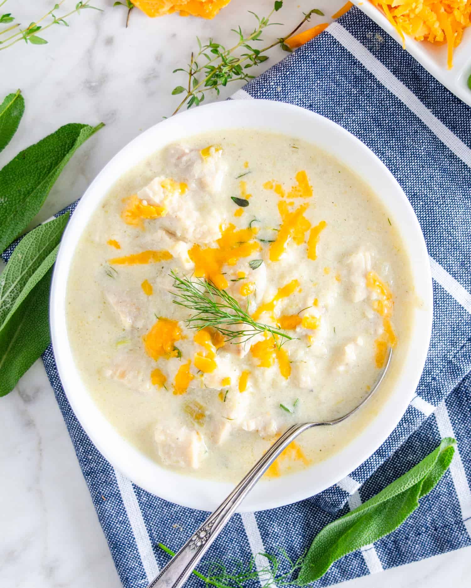 Low carb cauliflower soup in a white bowl garnished with cheddar cheese and thyme.