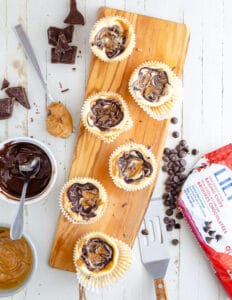 baked chocolate peanut butter keto cheesecakes on a wood board being unwrapped