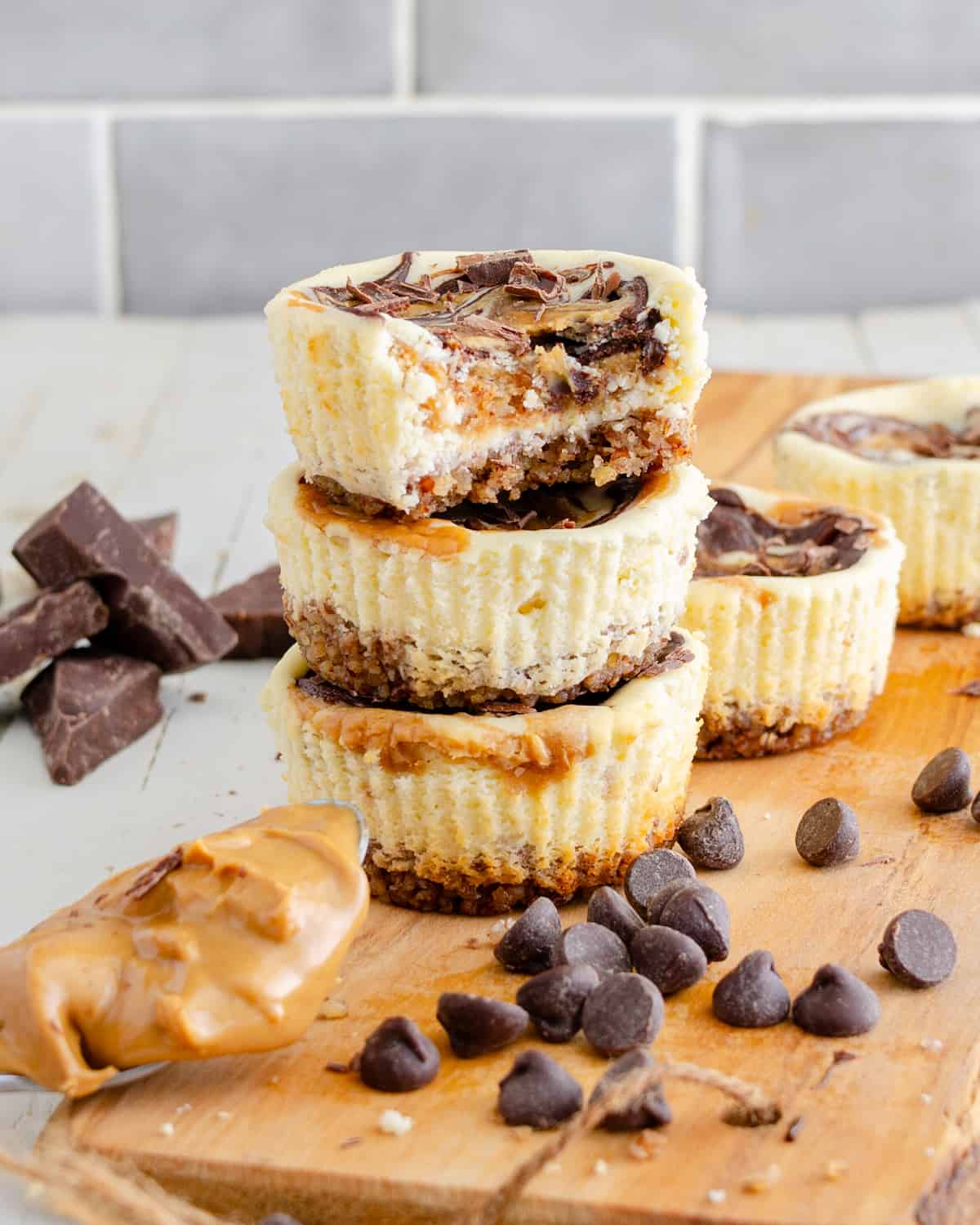 Mini muffin tin keto cheesecakes stacked on a wooden board with a bite out of them showing the chocolate and peanut butter inside.