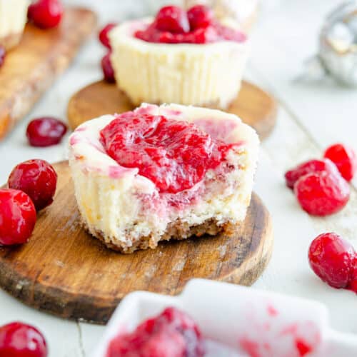 A cran raspberry mini keto cheesecake with a bite out of it on a wooden plate.