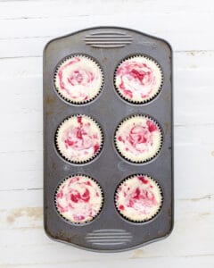 Baked keto mini cheesecakes swirled with raspberry in a muffin tin.