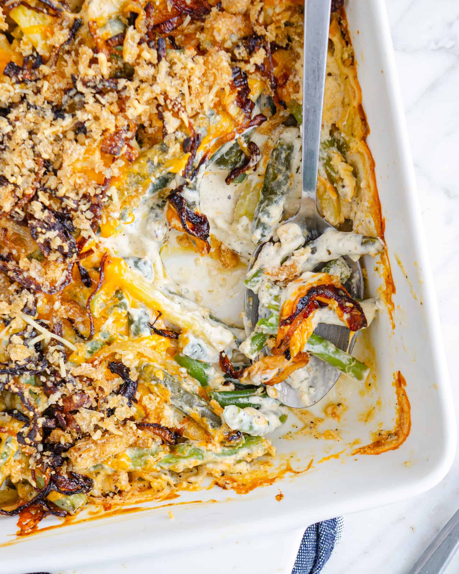 Keto green bean casserole in a white square serving dish with a scoop taken out showing the tender and green beans and cream cheese filling in the middle.