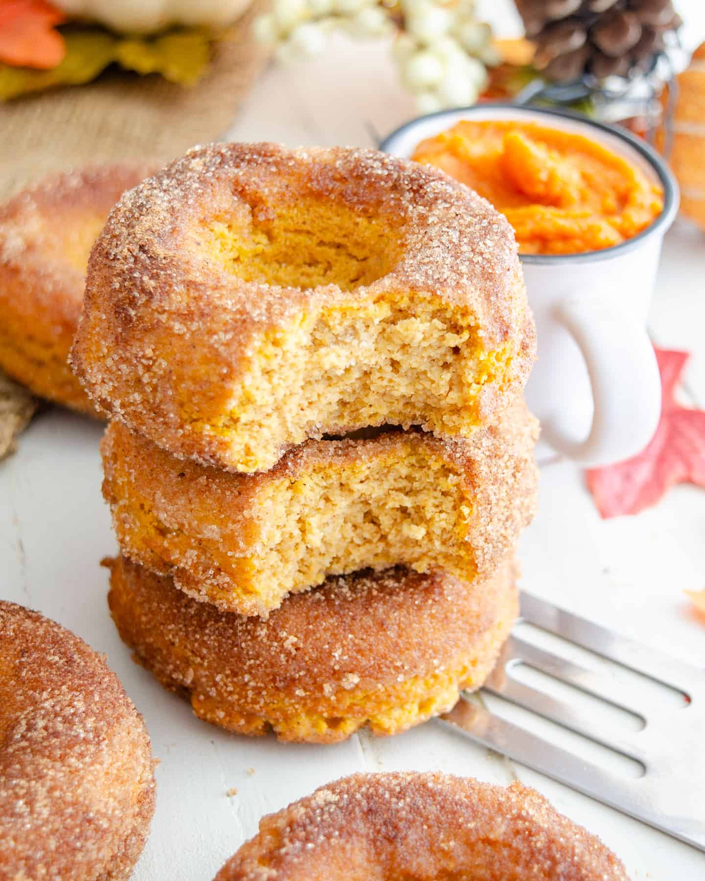A stack of baked keto pumpkin pie donuts with a bite out of them showing the cakey interior.
