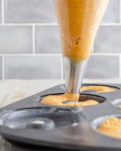 Pumpkin spice donut batter being piped into a donut pan.