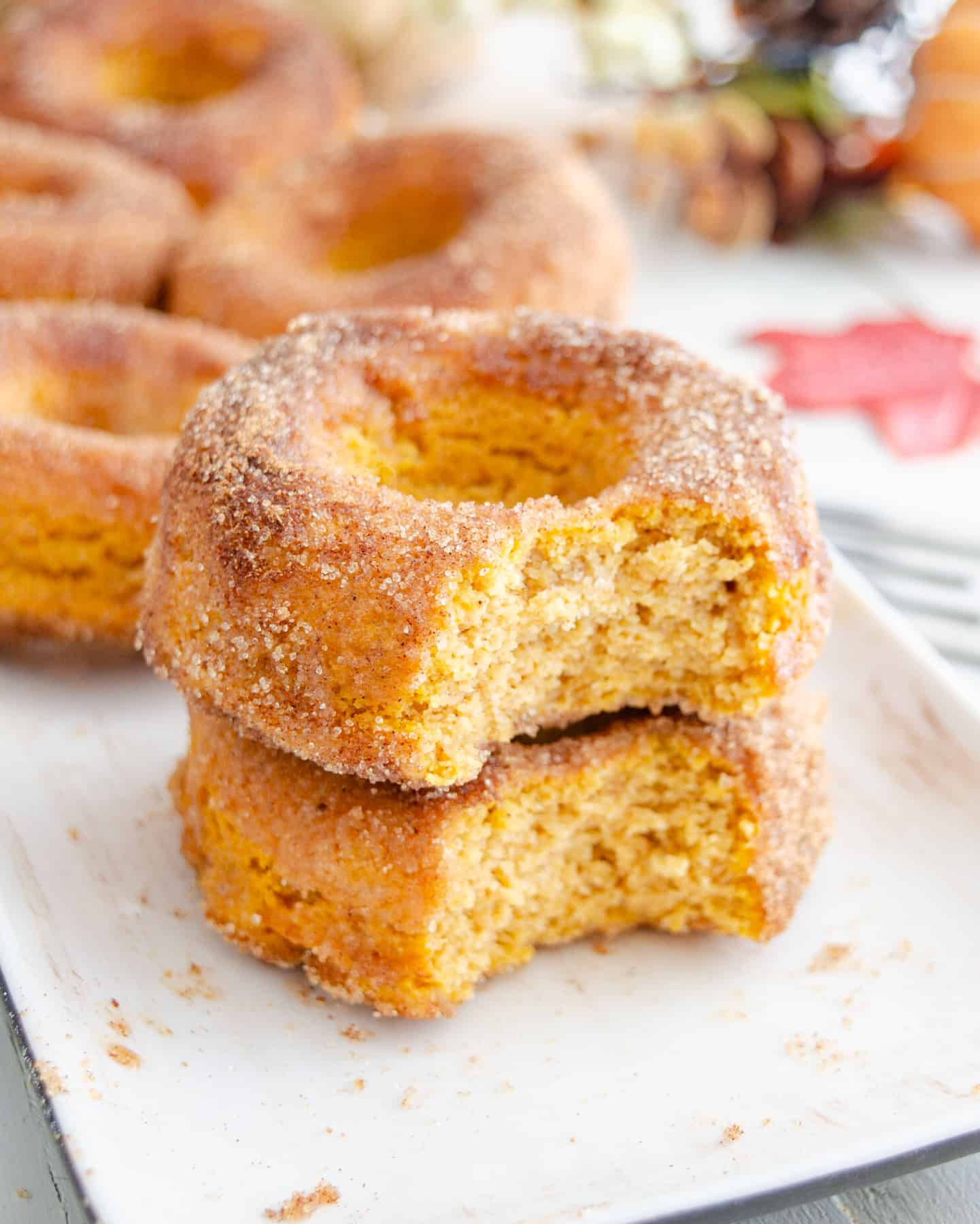 A stack of baked low carb pumpkin spice donuts with a bite out of them showing the cakey interior.