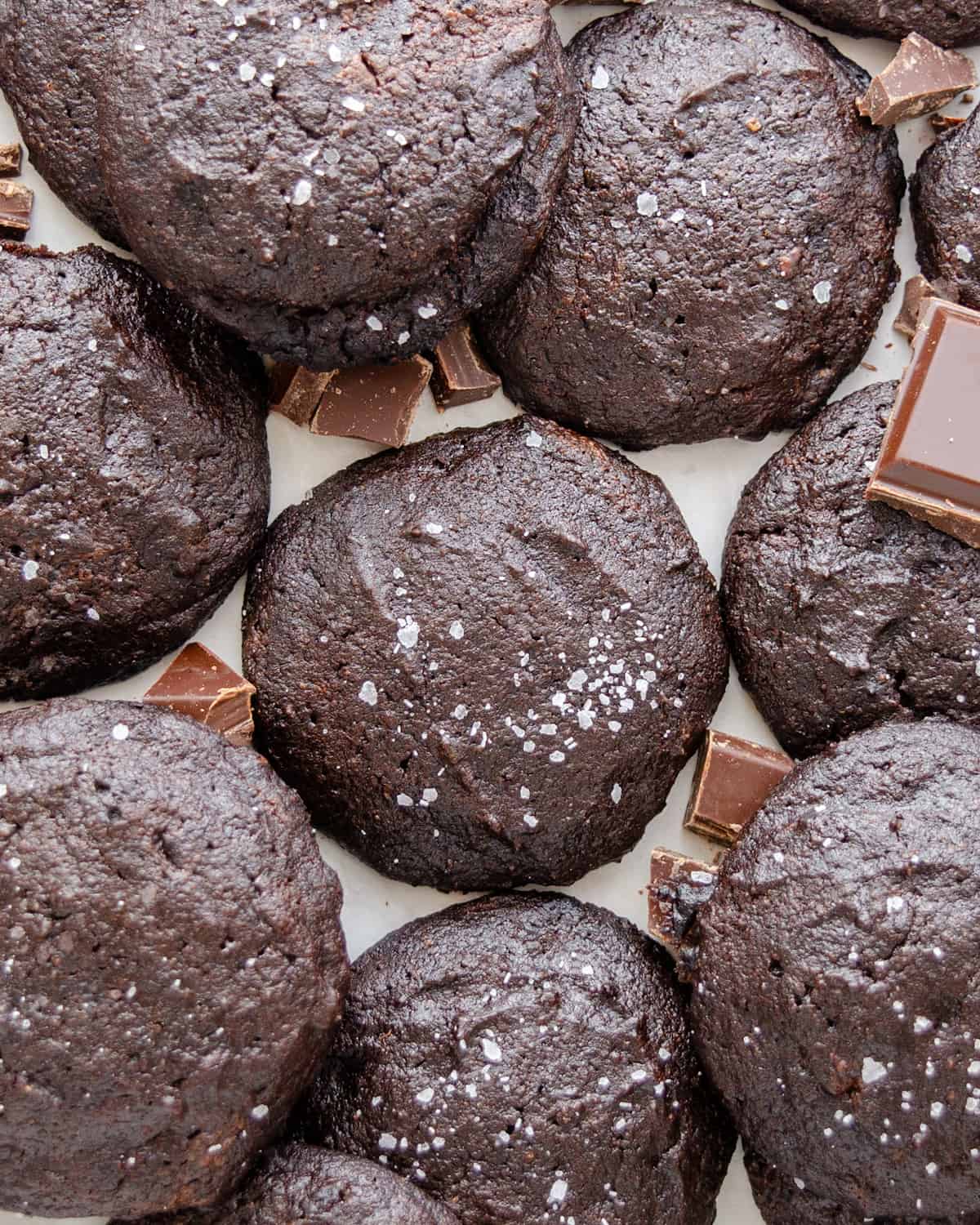Salted keto mocha brownie cookies on a white background with chopped chunks of chocolate.