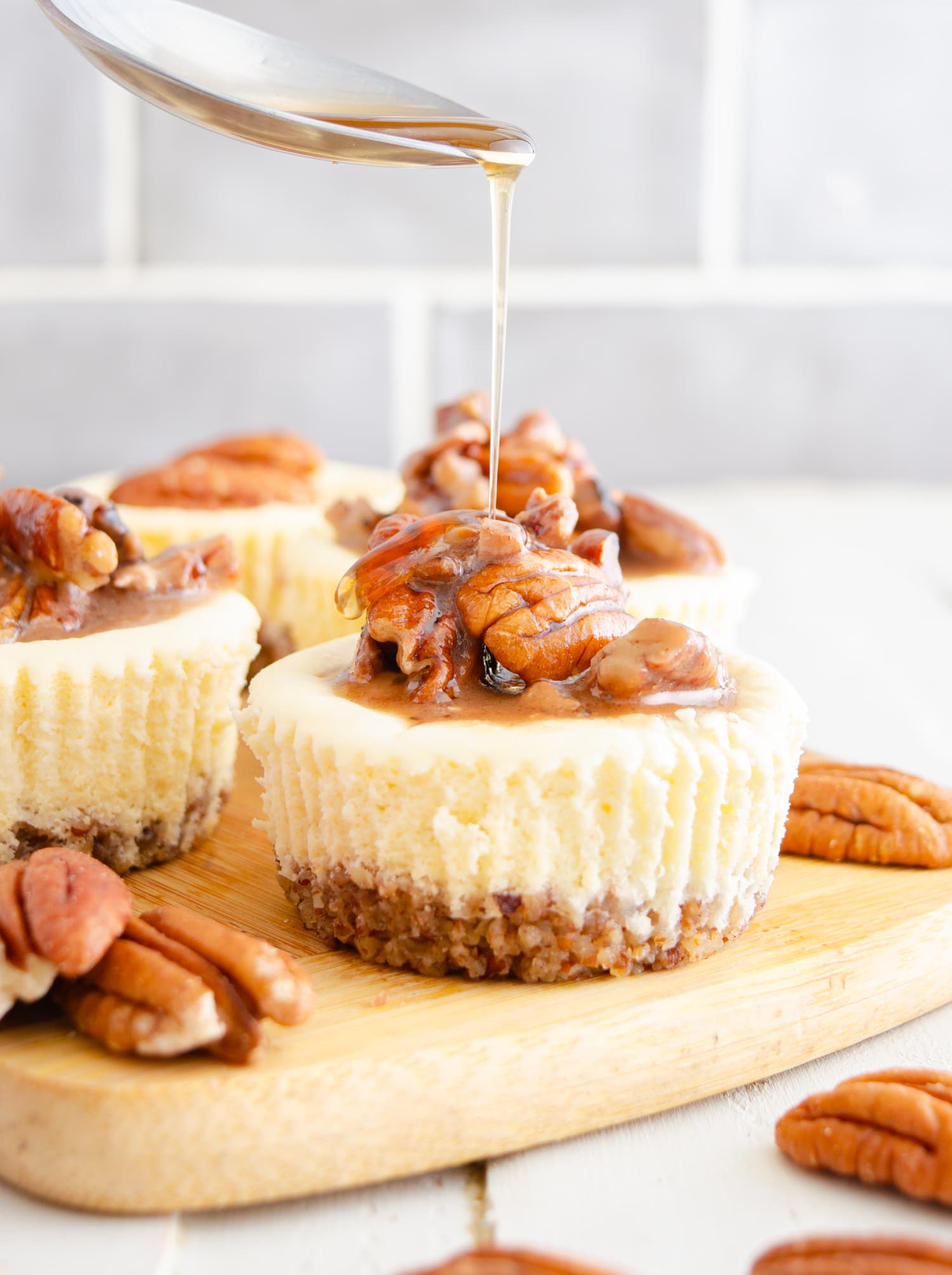 Mini keto cheesecakes topped with a sugar free maple pecan topping being drizzled with sugar free Walden's syrup.