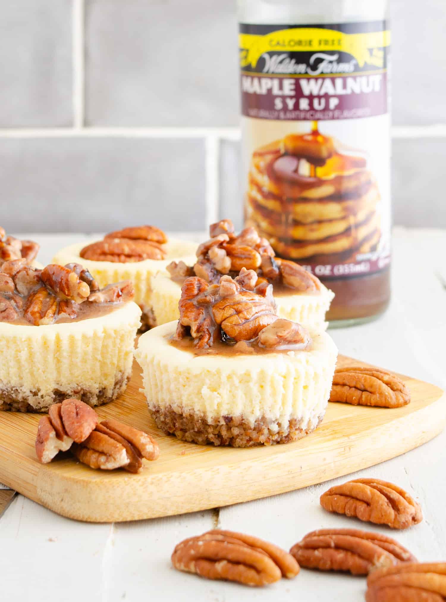 Mini keto cheesecakes with a sugar free topping maple from Waldens syrup and pecans. A bottle of Waldens in the background.