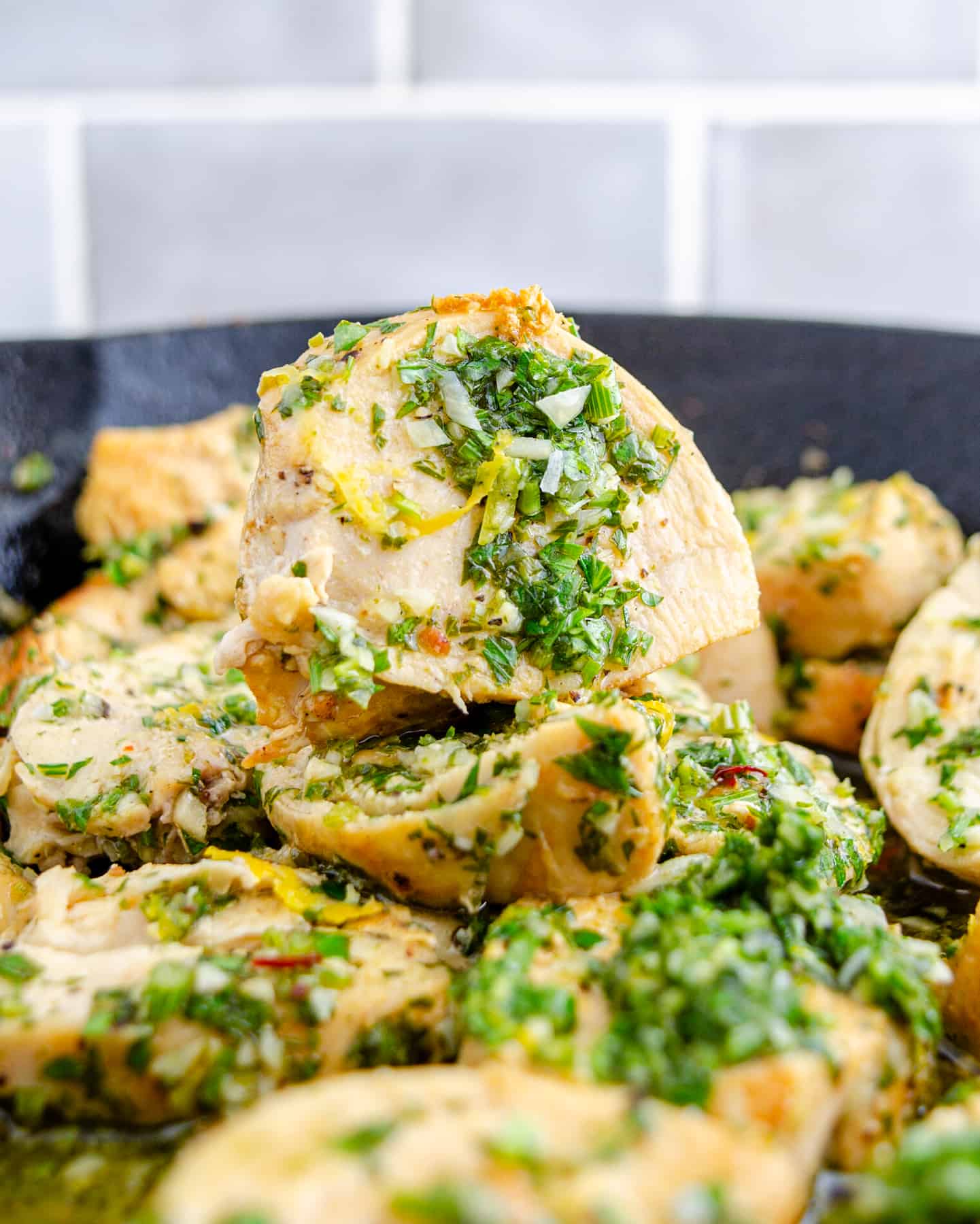 Pan seared pieced of chicken breast stacked in a cast iron skillet covered in Gremolata.