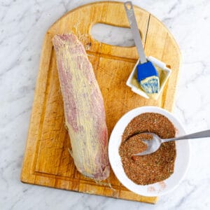 Mustard covered pork tenderloin on a cutting board.