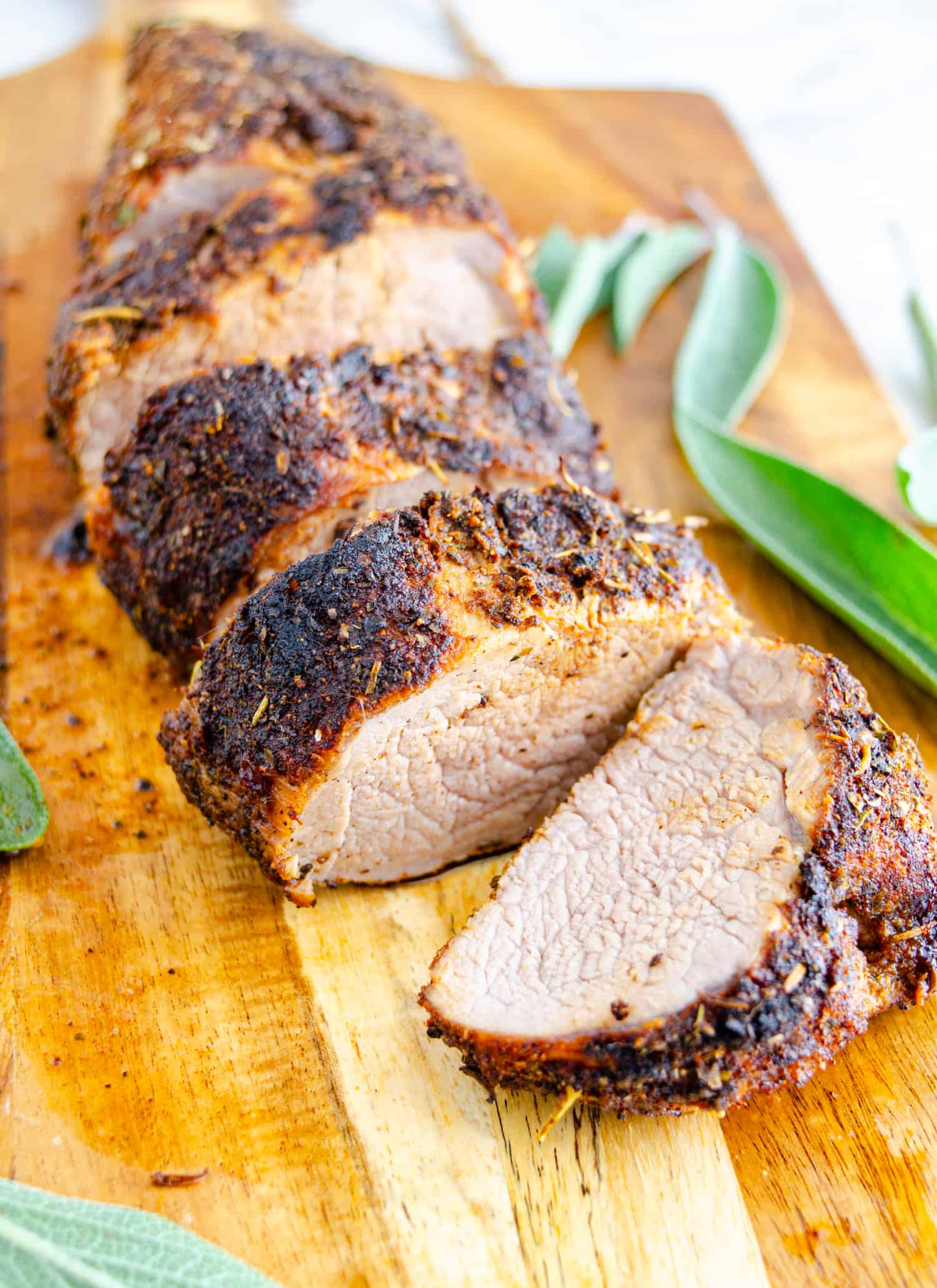 Sliced air fryer pork tenderloin with a caramelized spice rubbed crust on a wooden cutting board.
