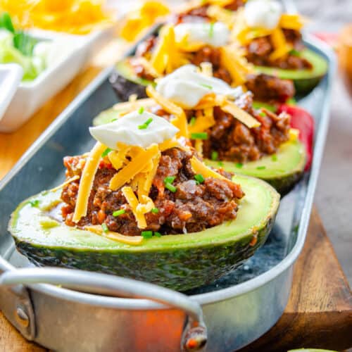 Chili cheese stuffed avocados fully loaded with cheese and sour cream on a metal tray.