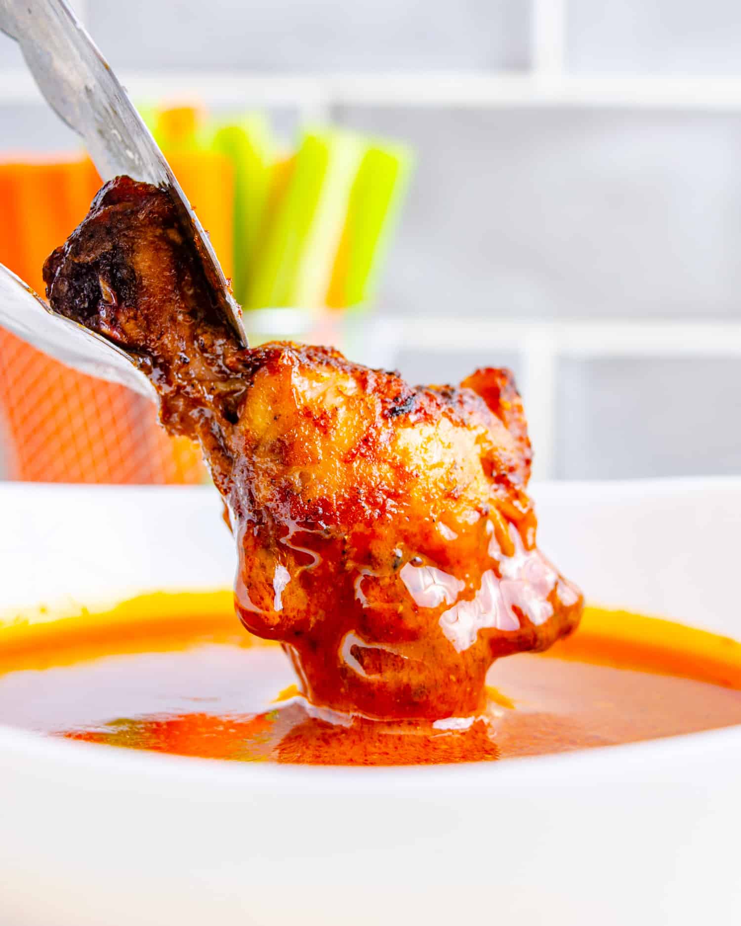 Dirty keto chicken wing being dipped into buffalo sauce.
