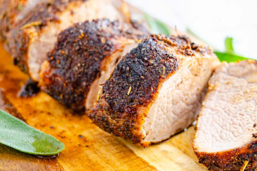 Sliced air fried pork tenderloin on a wooden board with a beautiful Spice rubbed crust.